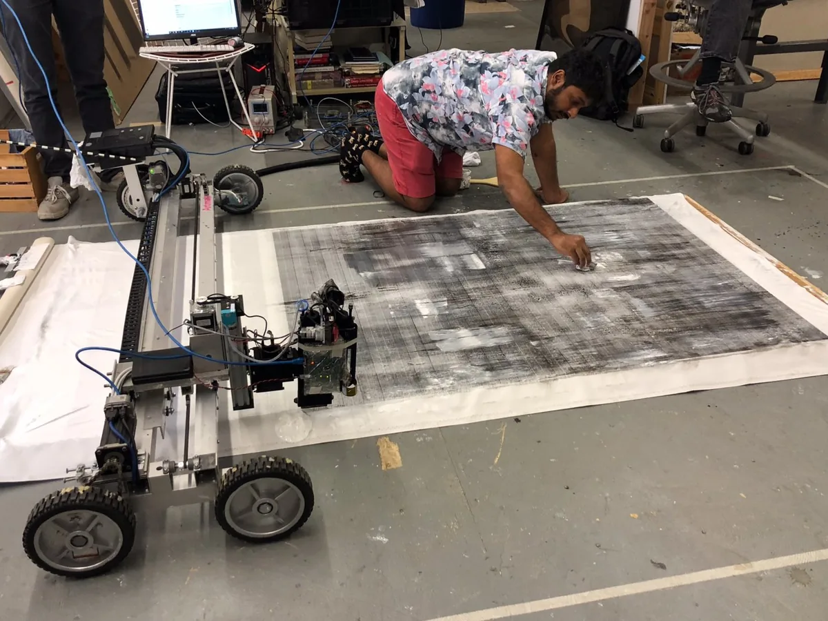Raghava KK working by hand on a large canvas beside a Matr machine